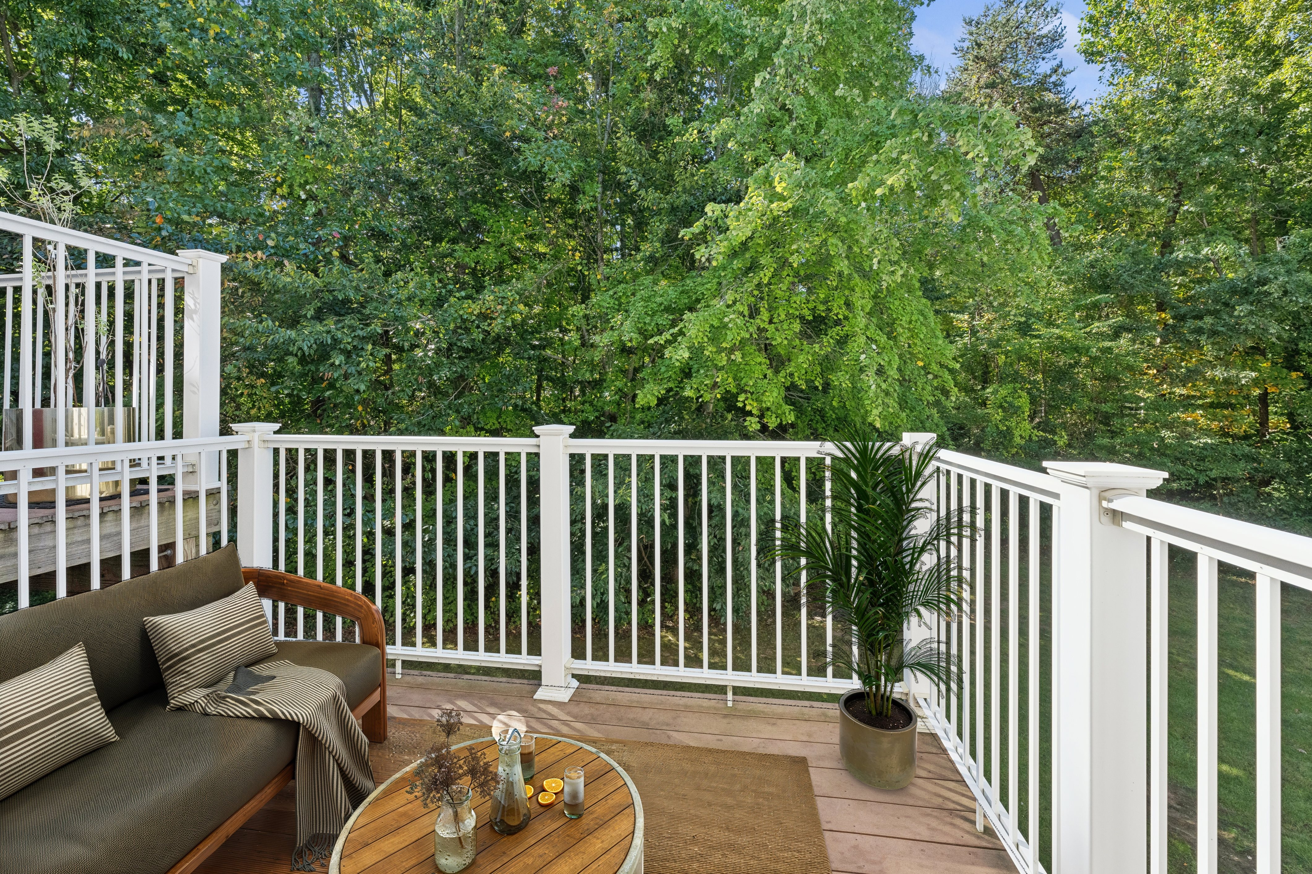 A white railing encloses a cozy balcony with a couch, table, and potted plant.